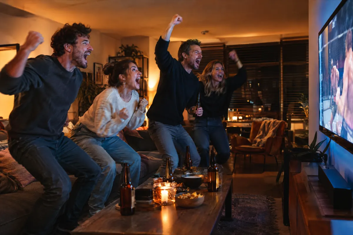 Vrienden springen juichend op van de bank tijdens een live vechtsportwedstrijd op tv